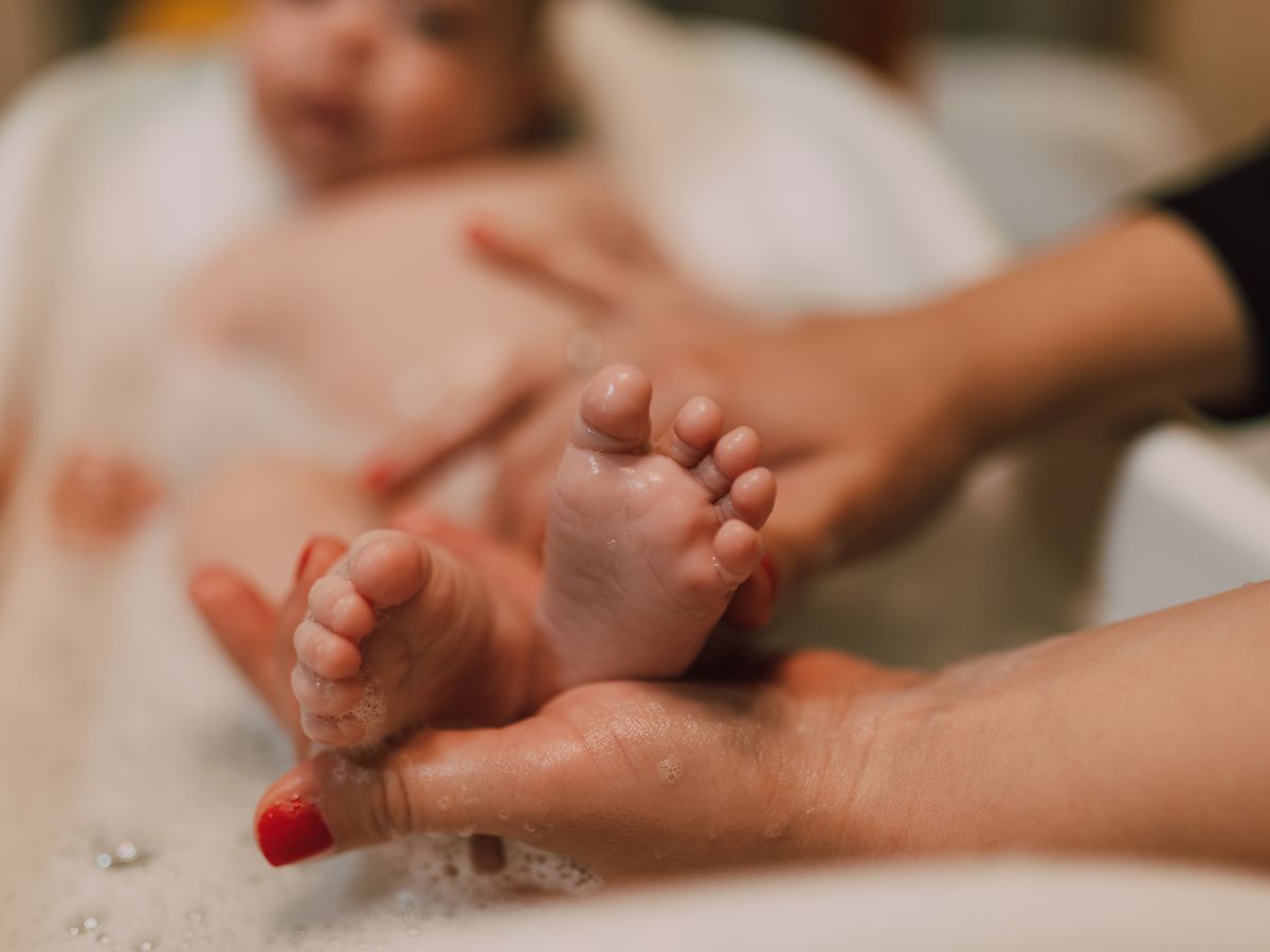 Pieds d’un bébé pendant le bain, soutenus par des mains d’adulte